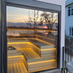 Moderna sauna po meri sa velikim staklenim izlogom i prijatnim LED osvetljenjem. Unutrašnjost saune je izrađena od kvalitetne kombinacije termičkog bora i abachi drveta, sa pogledom na zalazak sunca. Profesionalna izrada sauna za vaš wellness prostor.